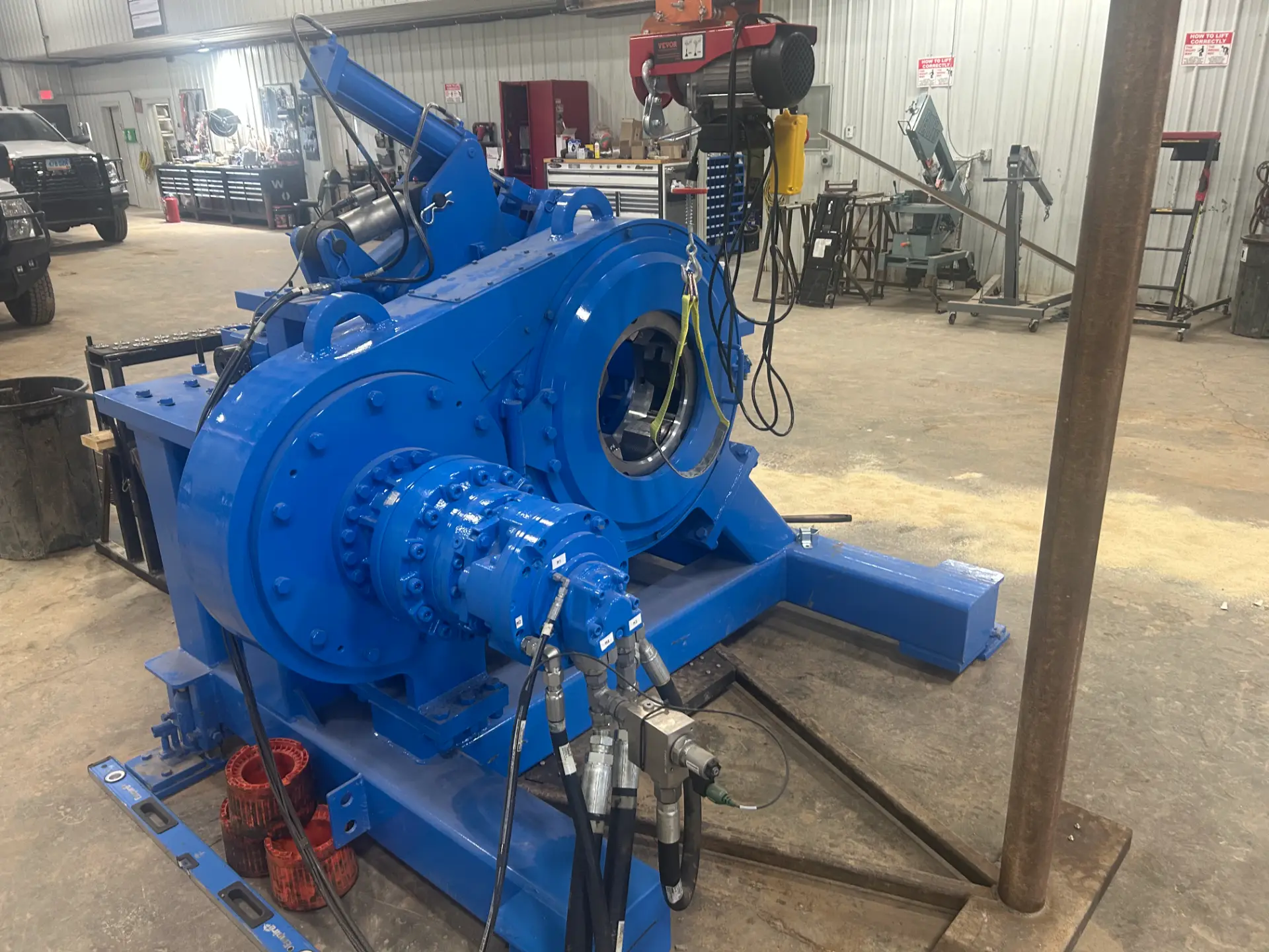 Blue NOV bucking unit head with rotating jaws and overhead chain hoist in the WOS shop