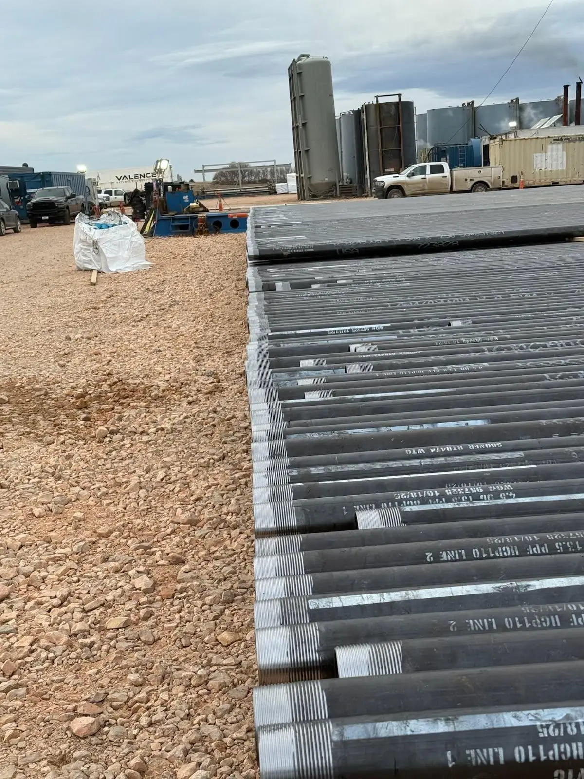 Casing pipe staged near production tanks and a Valence trucking trailer at a Bakken yard