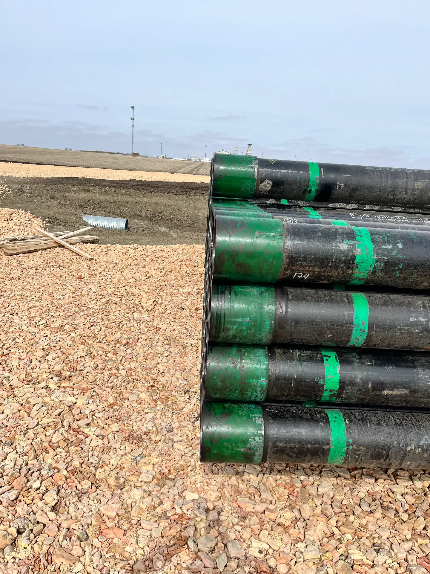 Stack of casing pipe with green couplings staged on a Bakken pad under an overcast sky