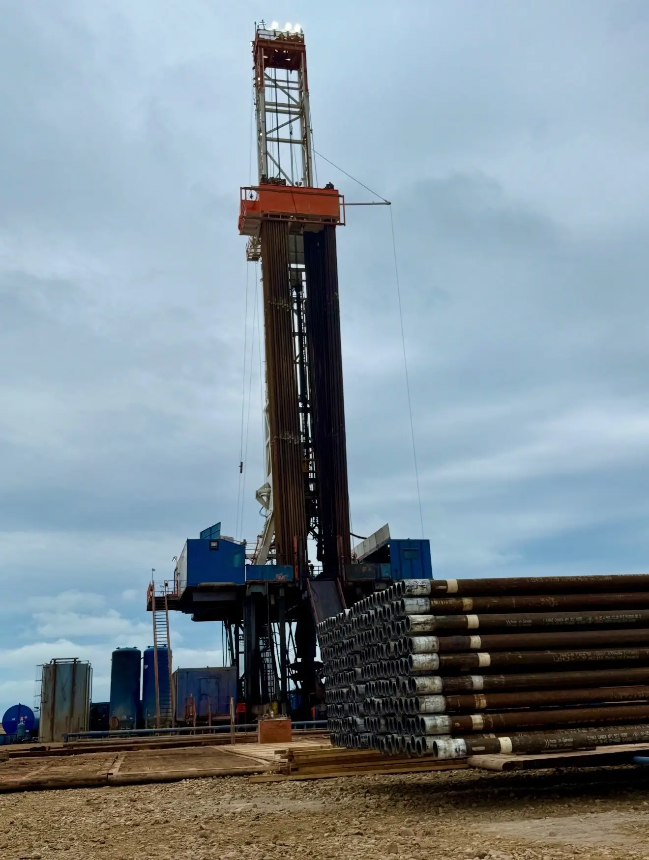 Workover rig towering above stacked casing pipe and frac tanks on a Bakken location