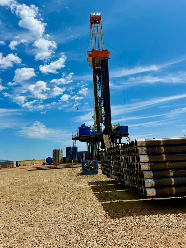 Workover rig with stacked casing on a Bakken location under partly cloudy skies