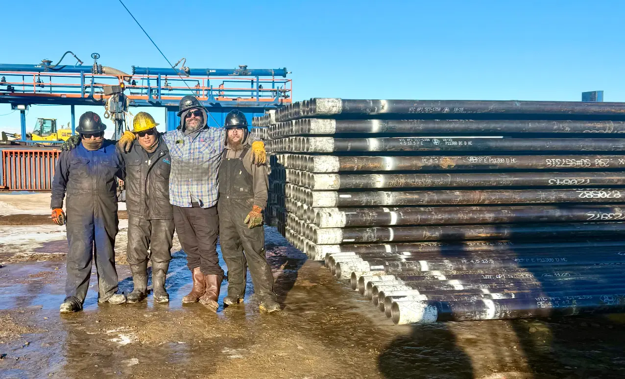 Four-man WOS casing crew posing in winter coveralls beside a stack of casing pipe