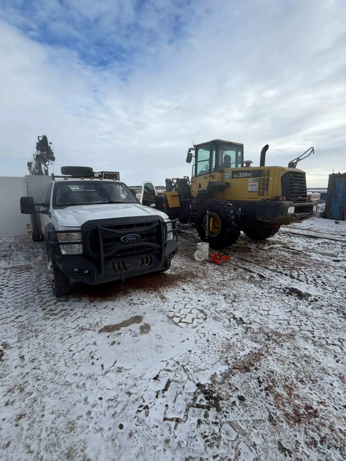 WOS Ford service truck and Komatsu wheel loader staged on a snowy Bakken yard