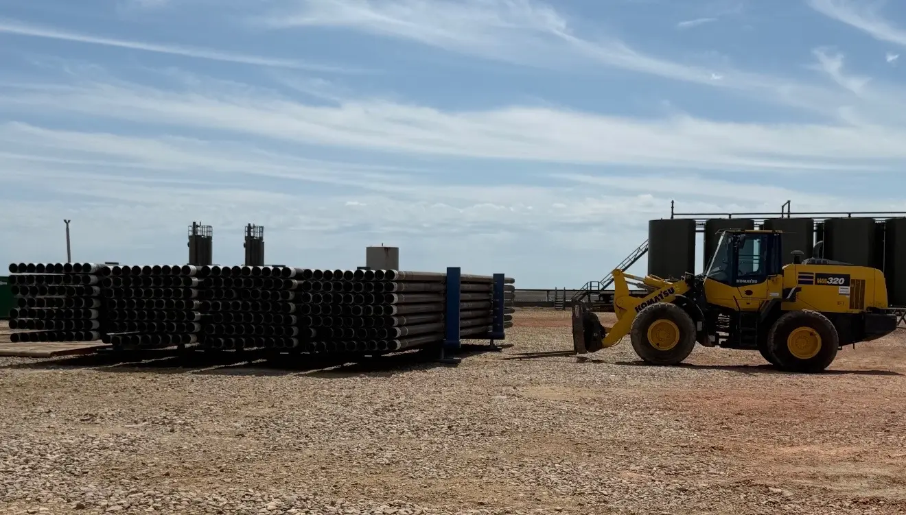 Stacks of drill pipe staged at a Bakken rig yard with a WOS wheel loader on standby