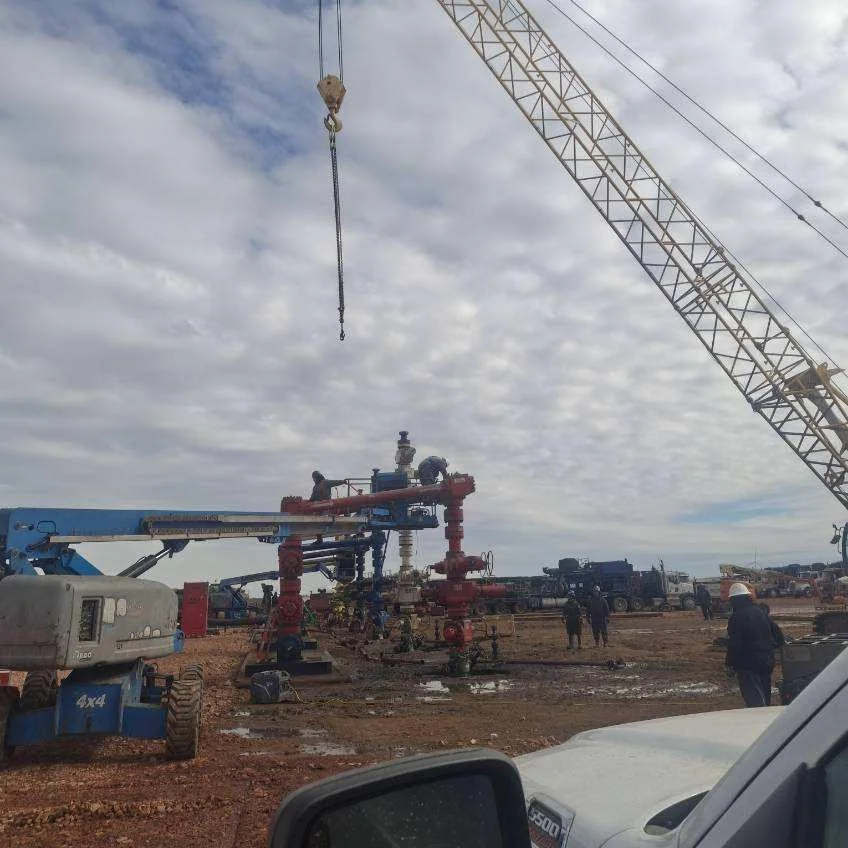 Pressure-test crew rigging up frac wellhead and iron under a workover crane on a Bakken pad