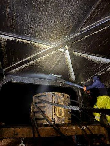 Worker pressure washing a rig component overhead