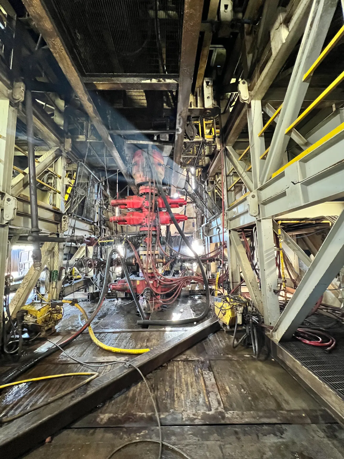 Crew pressure washing red BOP stack and rig floor under the substructure