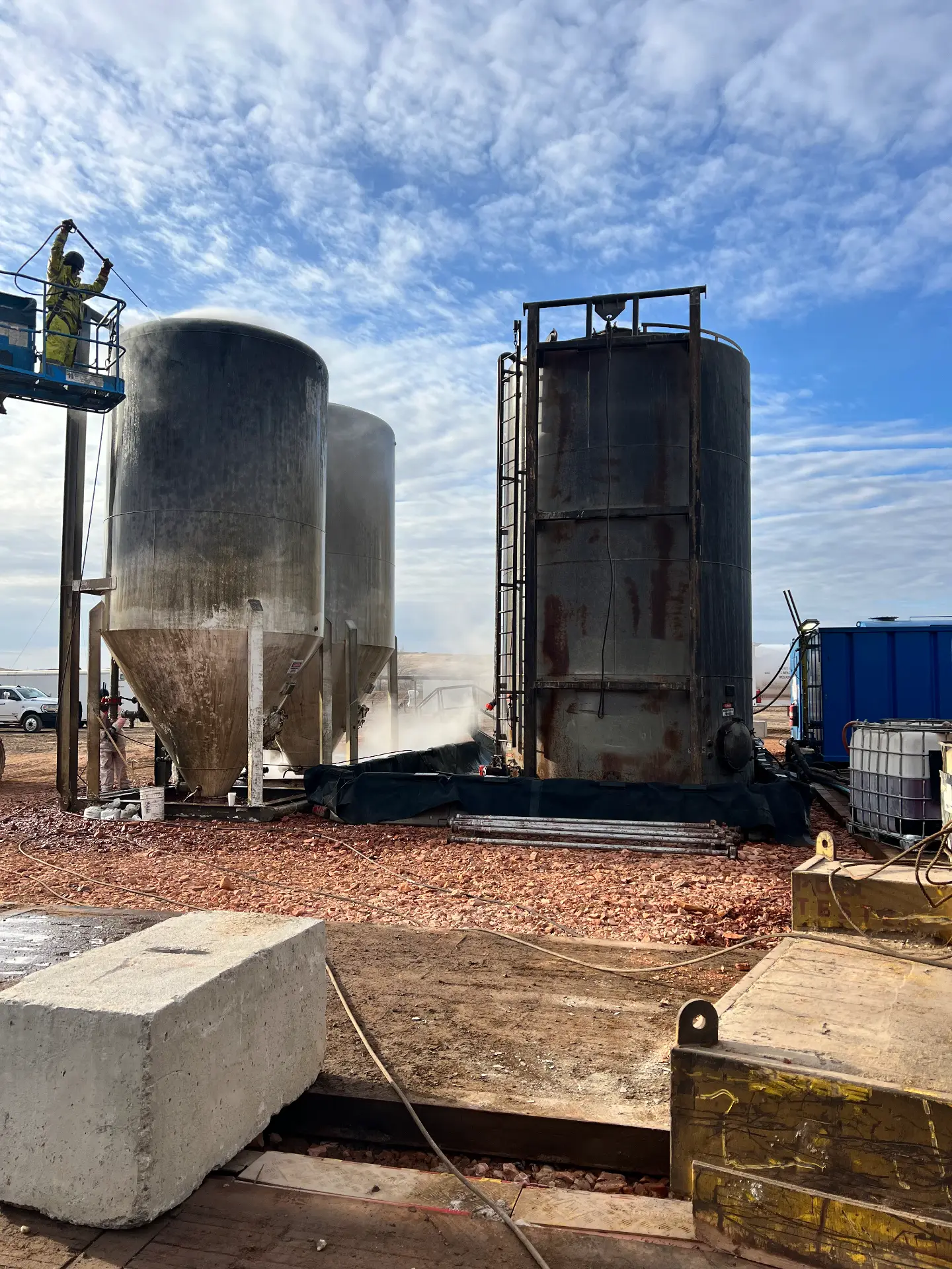 WOS technician on a man lift hot-water washing a tank battery on a Bakken pad