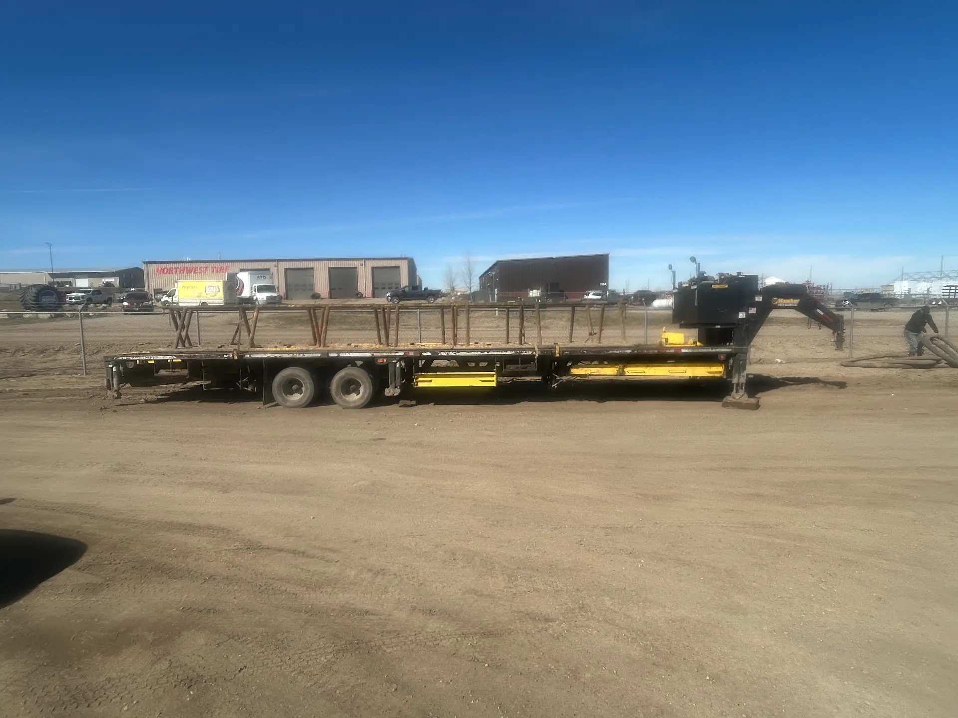 Gooseneck flatbed rental trailer loaded with pipe rack stands at the WOS yard