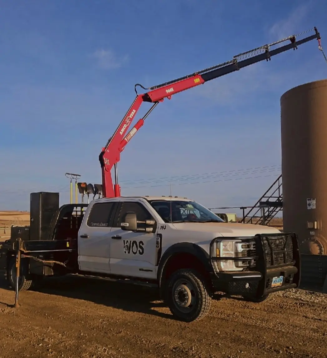 WOS knuckle boom truck staged next to a production tank on a Bakken location