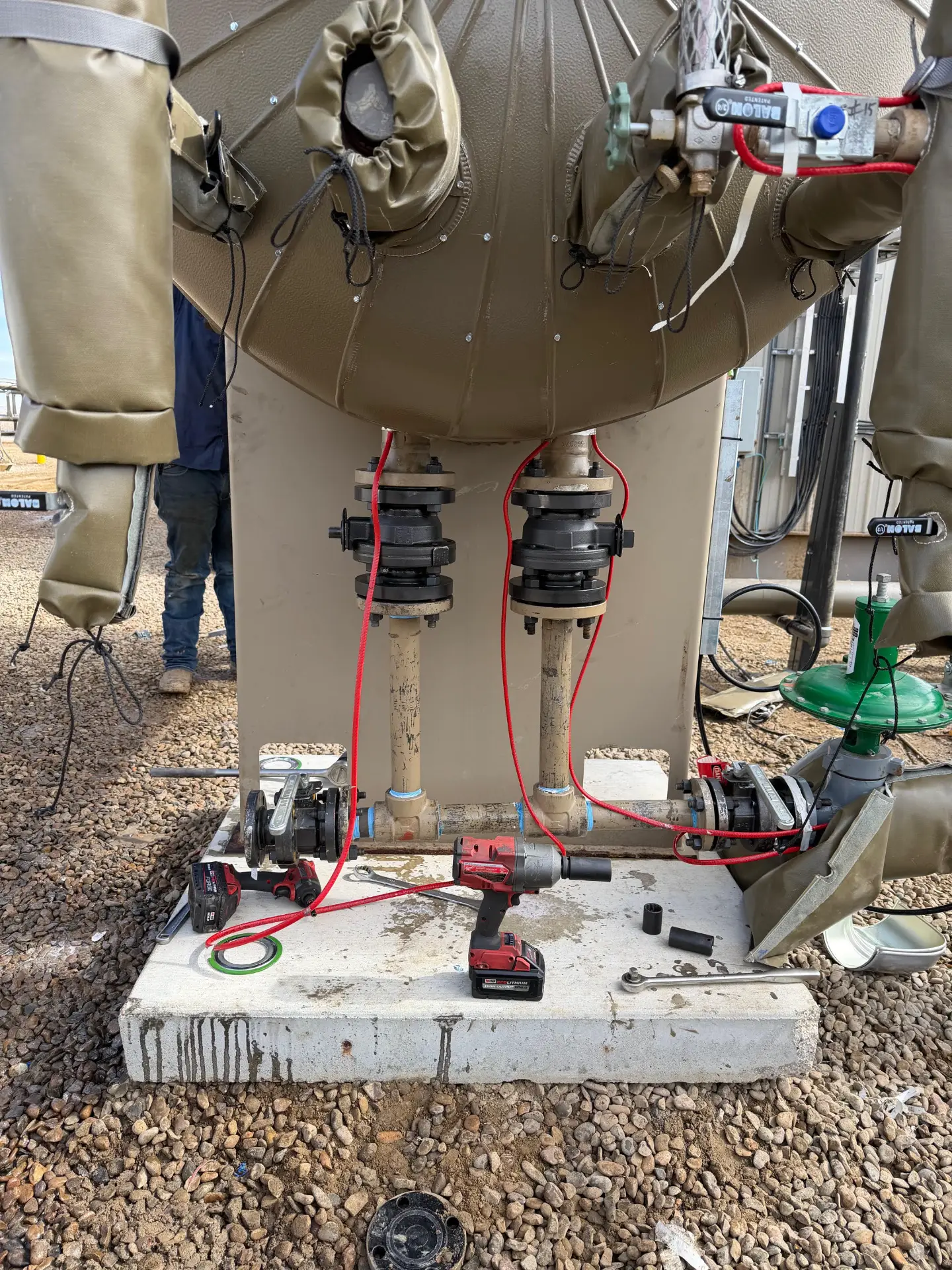 Close-up of a treater base with valves, red-banded piping, and impact tools during facility service