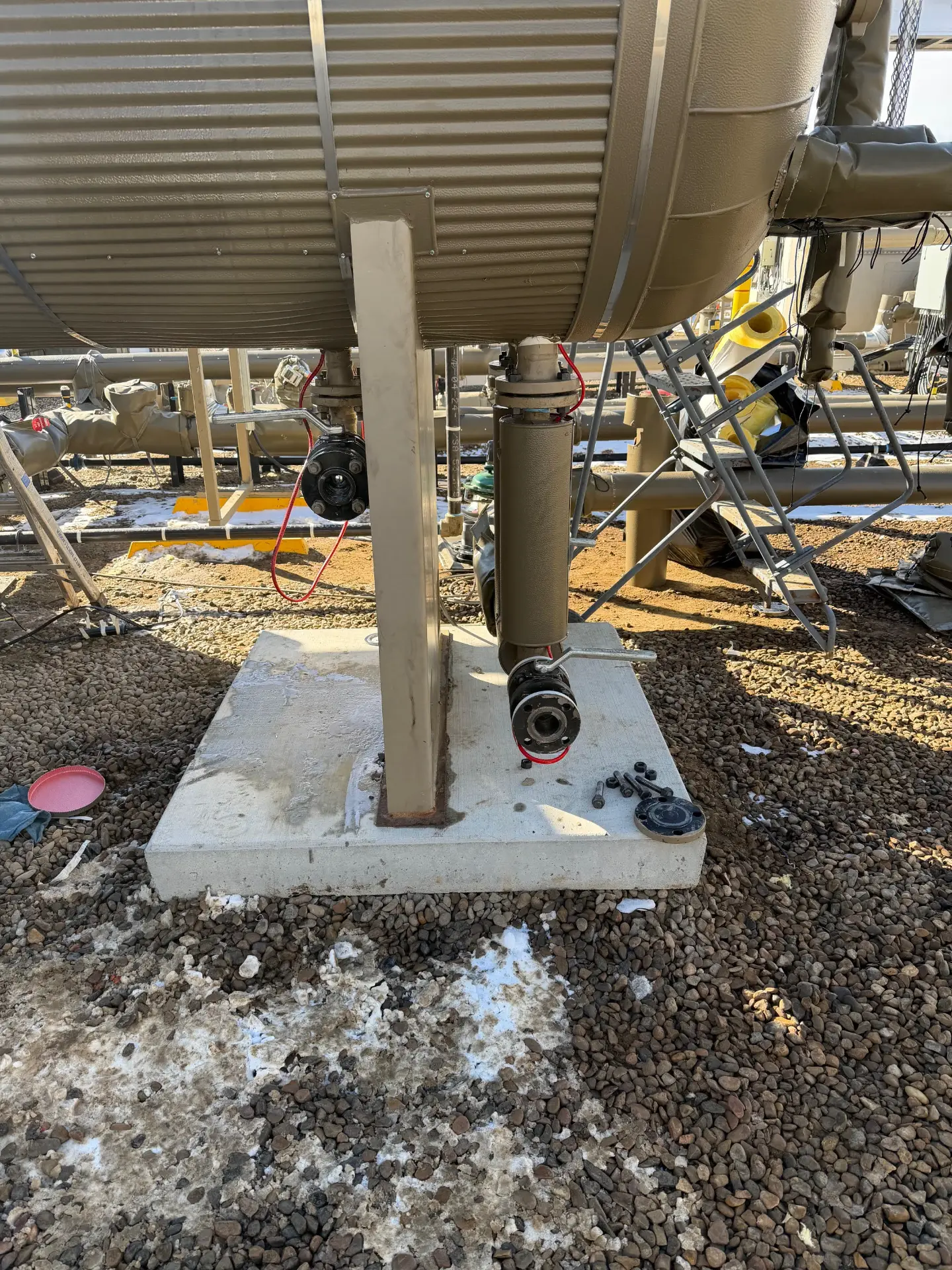 Underside of a production tank with valves and piping mounted on a concrete pad