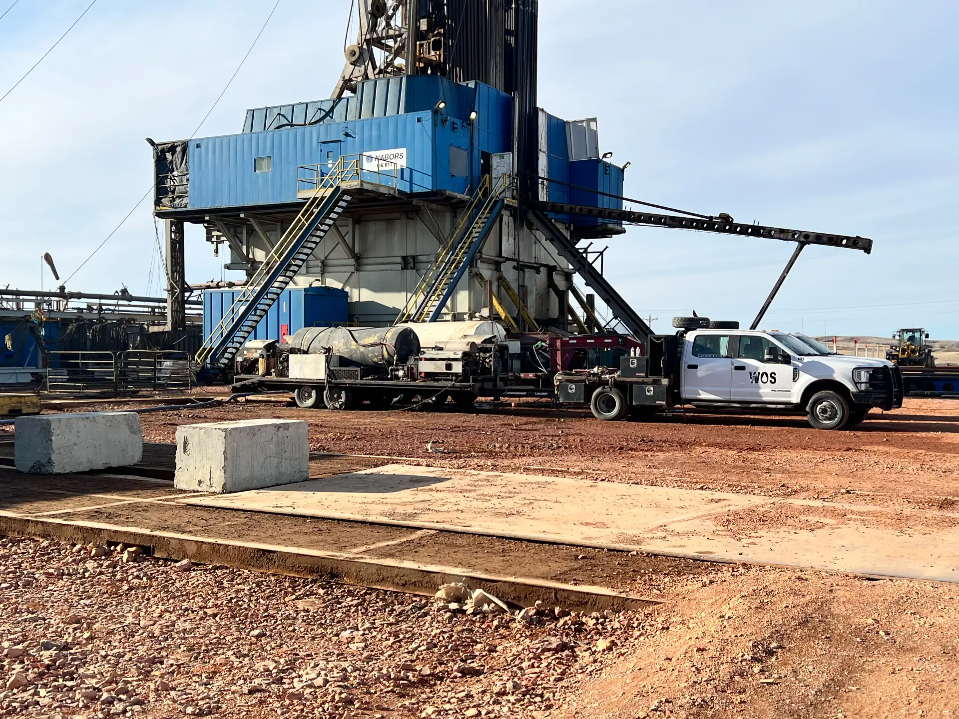 WOS service truck staged next to a Nabors workover rig substructure on a Bakken pad