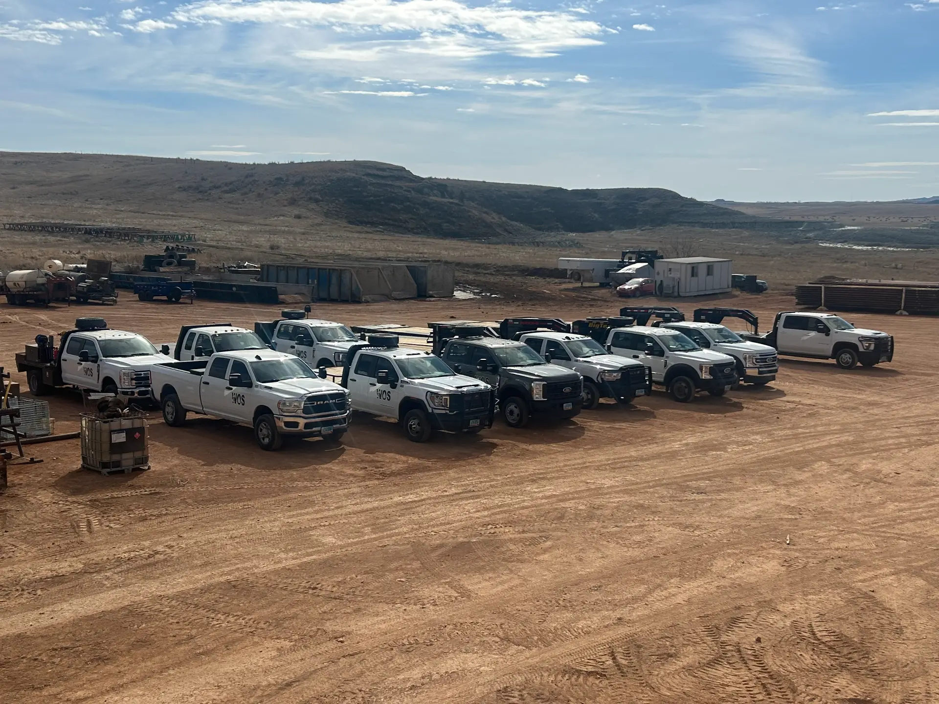 Overhead view of WOS pickups, flatbeds, and a knuckle-boom truck lined up outside the Williston shop