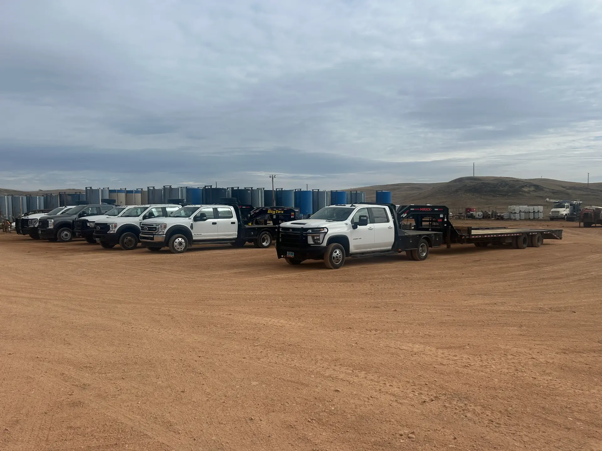 WOS service truck fleet and gooseneck trailer parked in front of a production tank battery